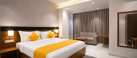 Una habitación de hotel moderna con una cama grande, mesitas de noche, un sofá, un espejo y un ventilador de techo.