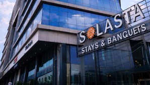 A tall building with a clear sky and sun. The building has a sign that reads 'SASTA STAYS & BANQUETS'. - Solasta Stays & Banquets - Wakad (Tathawade)