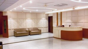A modern lobby with a reception desk, two sofas, and a large mirror. - Solasta Stays & Banquets - Wakad (Tathawade)