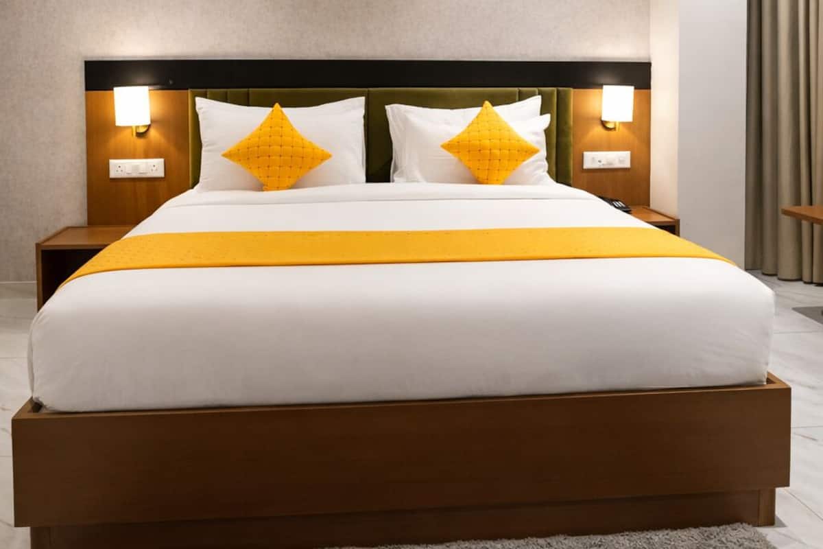 Una cama grande con estructura de madera, dos mesitas de noche con lámparas, un ventilador de techo y una alfombra gris.