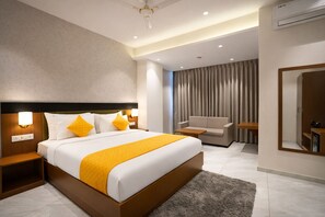 A modern hotel room with a large bed, a sofa, a desk, and a mirror.