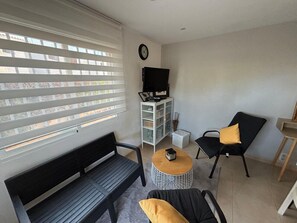 Een knus zithoekje met een bank, twee fauteuils, een salontafel, een televisie en een kast.