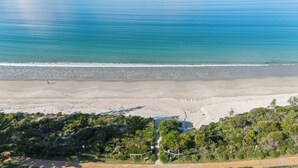 Een strand met een helder uitzicht over de oceaan, een zandstrand en weelderige begroeiing op de voorgrond.