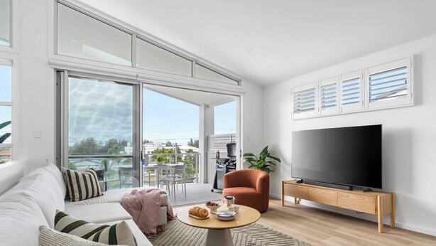 Een moderne woonkamer met een bank, een bijzettafeltje, een televisie en een balkon met tuinmeubilair.