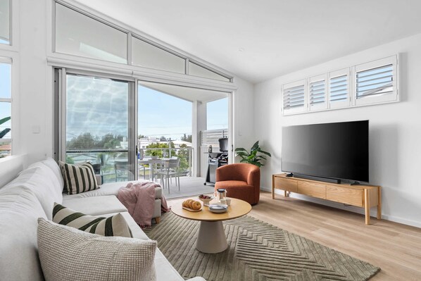 A modern living room with a sofa, a coffee table, a TV, and a balcony with outdoor furniture. - Kaze South in Vincentia (Vincentia)