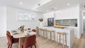 Een moderne keuken met witte kastjes, een centraal kookeiland met krukken, en een eethoek met een tafel voor vier personen.