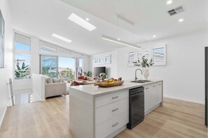 A modern kitchen with a central island, white cabinetry, and a black dishwasher. - Kaze South in Vincentia (Vincentia)