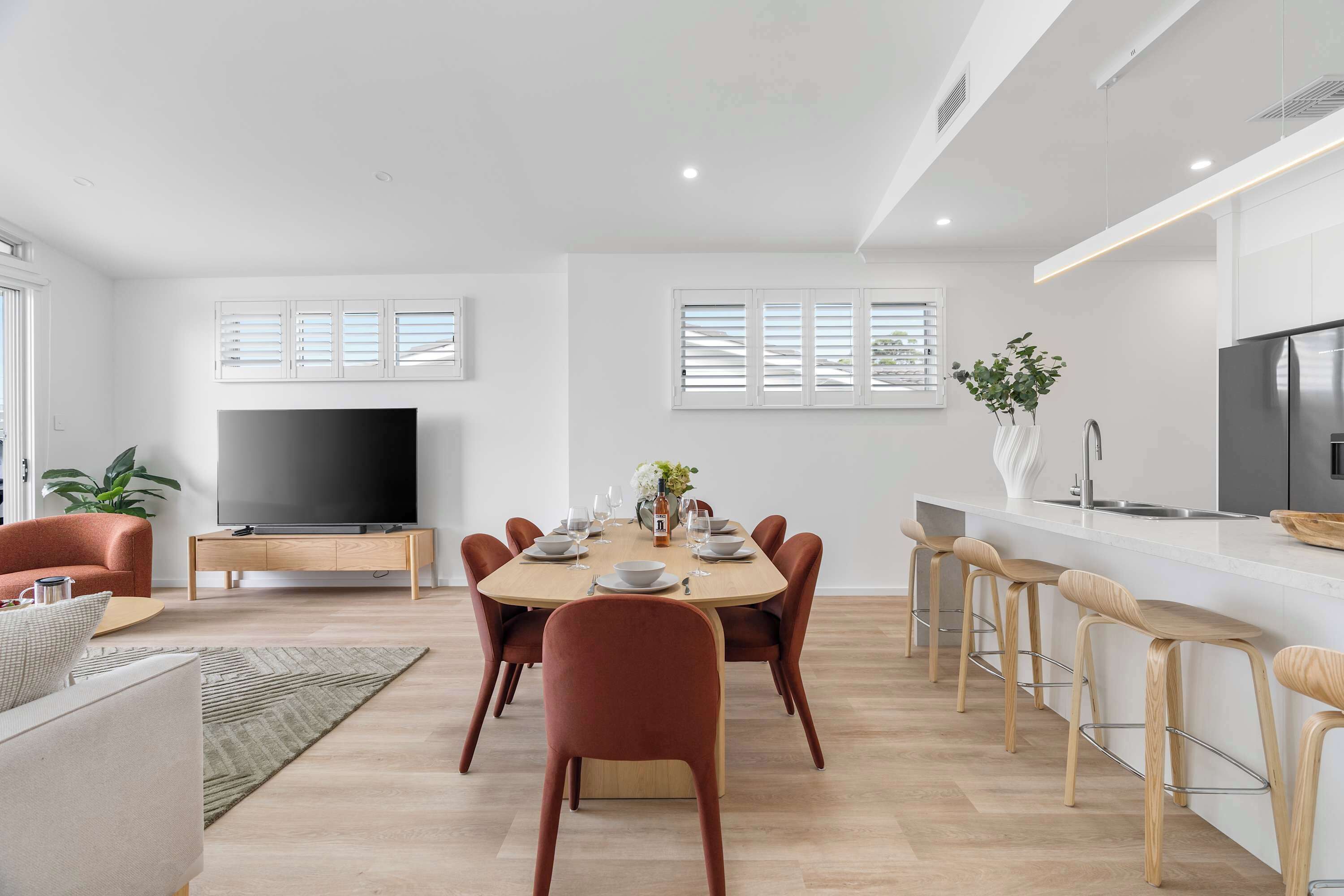 Una sala de estar moderna con comedor, televisor de pantalla plana y cocina con refrigerador de acero inoxidable.