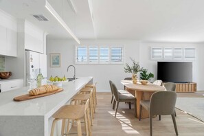 Eine moderne Küche mit Kochinsel, Holzkästen, einem Esstisch und einem Flachbildfernseher in einem hellen Wohnbereich.