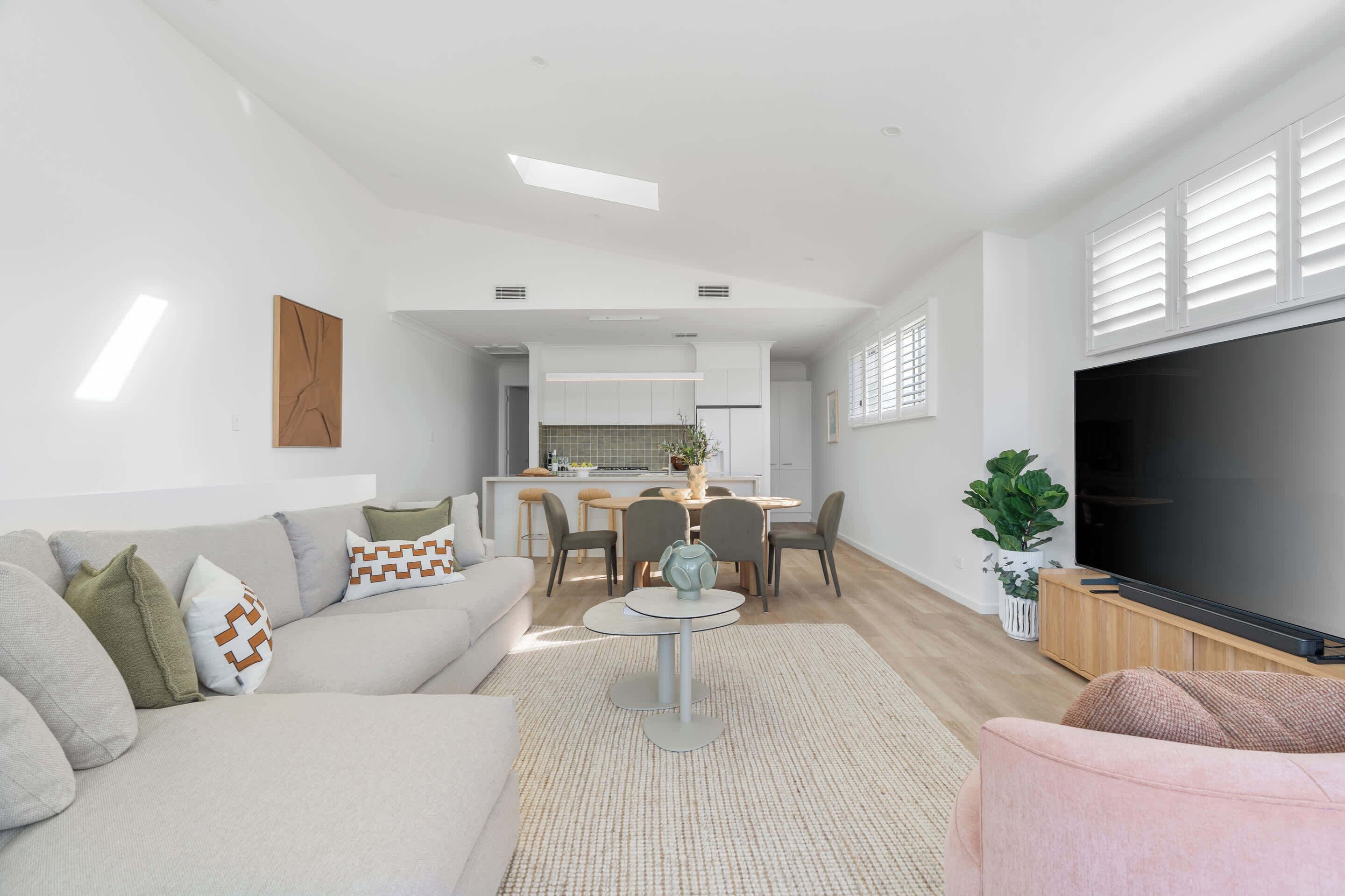 A modern living room with a sofa, coffee table, and TV. There is a dining area with chairs and a table in the background.
