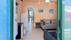 A living room with a sofa, a television, and a kitchen area visible through an open doorway. - Charming apartment in quaint Gastouri perfect for relaxing getaway (Gastouri)