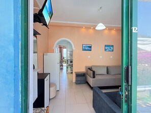 A modern living room with a sofa, a television, and a kitchen area visible through an open door. - Charming apartment in quaint Gastouri perfect for relaxing getaway (Gastouri)