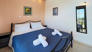 A neatly made bed with white and blue bedding, two white towels, and a painting on the wall. - Charming apartment in quaint Gastouri perfect for relaxing getaway (Gastouri)