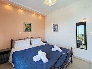 A neatly made bed with white and blue bedding, two white towels, and a painting on the wall. - Charming apartment in quaint Gastouri perfect for relaxing getaway (Gastouri)