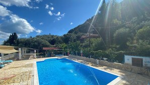 A swimming pool with a stone deck, a children's play area, and a view of a mountainous landscape. - Charming apartment in quaint Gastouri perfect for relaxing getaway (Gastouri)
