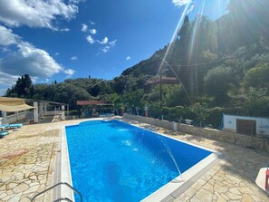 A swimming pool with a stone deck, a children's play area, and a view of a mountainous landscape. - Charming apartment in quaint Gastouri perfect for relaxing getaway (Gastouri)