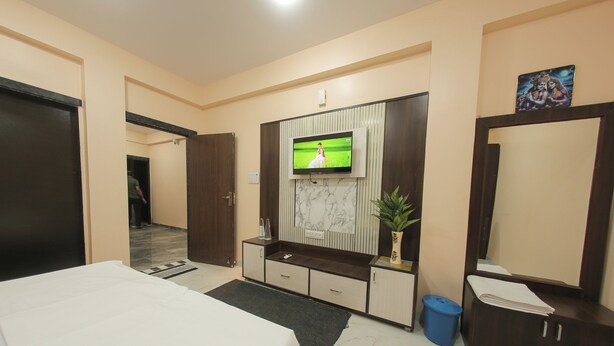 A hotel room with a bed, a TV mounted on the wall, a desk with drawers, a mirror, and a potted plant. - Tulsi Leela - Home Stay (Dr. Ambedkar Nagar)