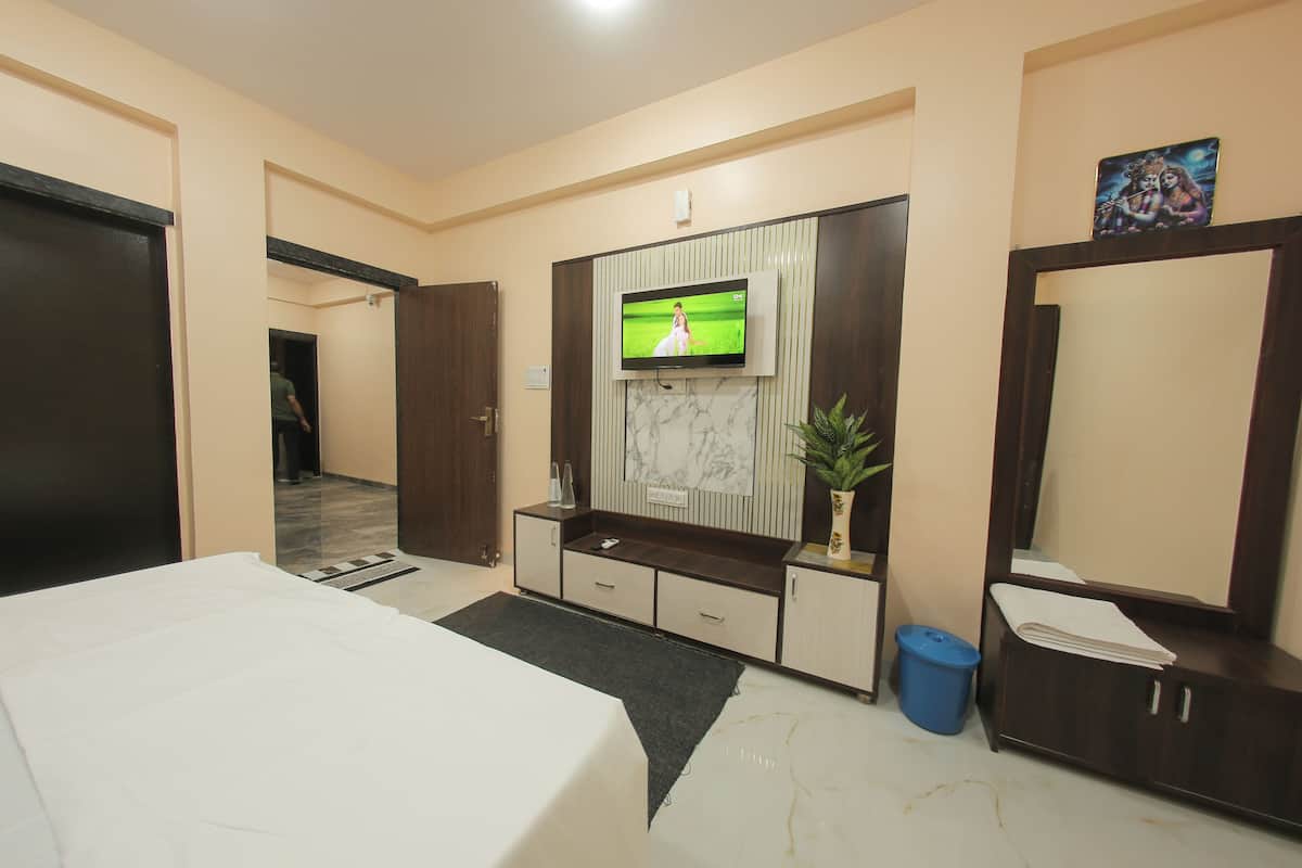 A hotel room with a bed, a TV mounted on the wall, a desk with drawers, a mirror, and a potted plant.