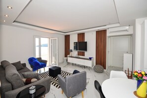 Ein modernes Wohnzimmer mit Sofa, Couchtisch, Fernseher und einem Essbereich mit Tisch und Stühlen.