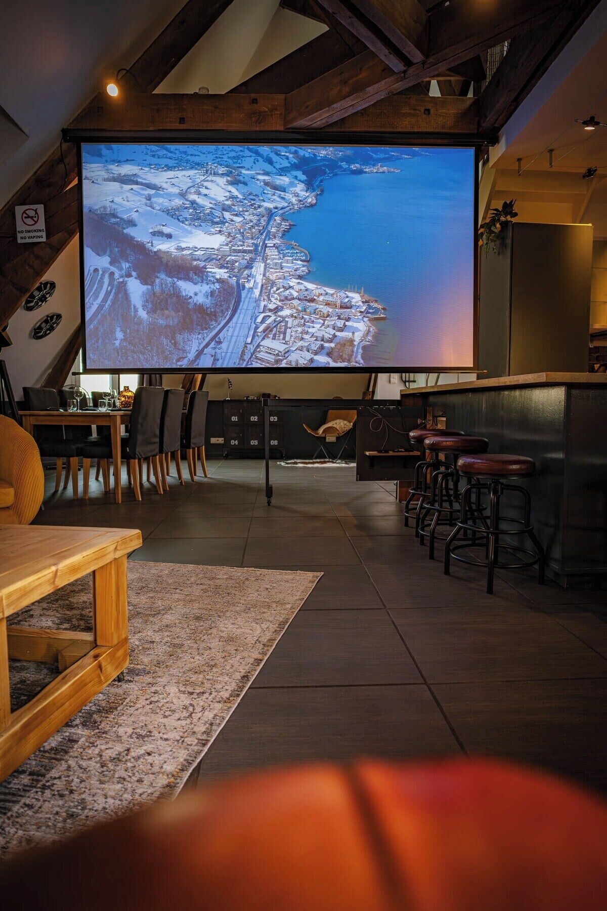 A cozy room with a large screen displaying a snowy landscape, wooden furniture, and a bar area.