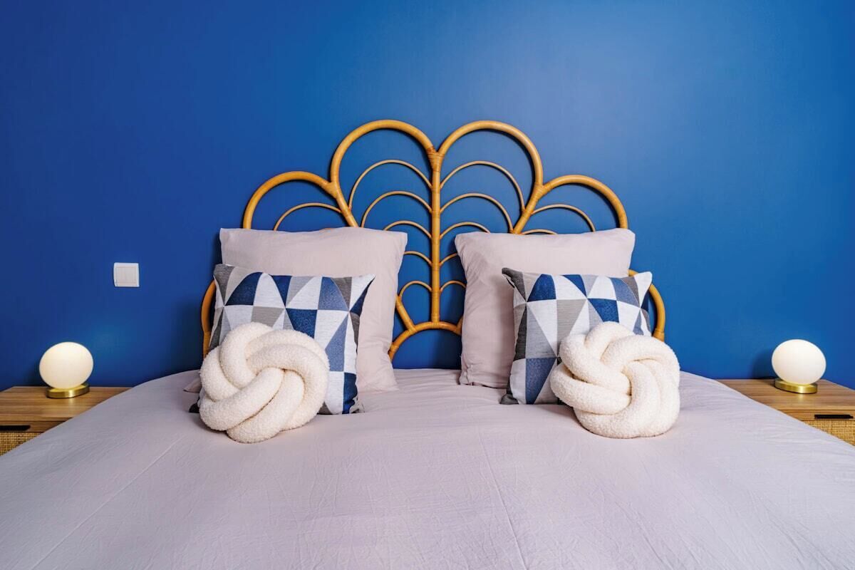 A bed with a blue headboard, two patterned pillows, and two white, twisted decorative pillows.