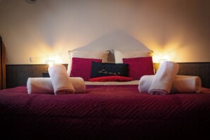 A neatly made bed with a red and white bedspread, two rolled towels, and a pillow with the word 'Love' on it. - British Style, projector, foosball & right in the heart of downtown (Le Mans)