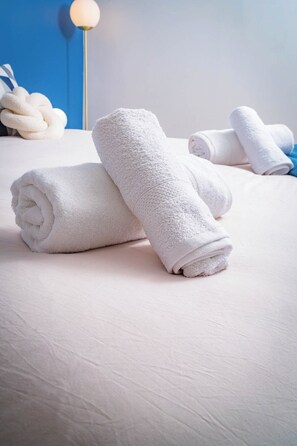 A neatly made bed with rolled white towels, a blue wall, and a floor lamp in the background. - British Style, projector, foosball & right in the heart of downtown (Le Mans)