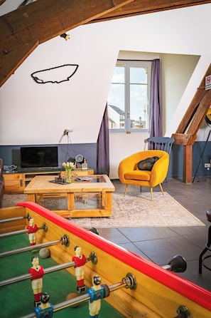 Un espai tipus loft amb sostre de fusta, un sofà, una taula de cafè, una taula de futbolí i una finestra.