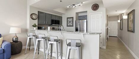 A modern kitchen with a central island, bar stools, and a dining area with a sofa and lamp.
