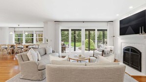 A spacious living room with a fireplace, large windows, and a dining area.