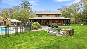 A two-story house with a brick exterior, a covered patio, a swimming pool, and a well-maintained lawn.