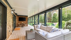 A covered patio with a sofa, a table, and chairs, and a view of a garden.