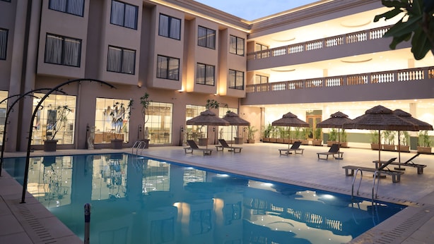 Un hôtel doté d’une piscine, de chaises longues, de parasols et d’un immeuble à plusieurs étages avec des balcons.