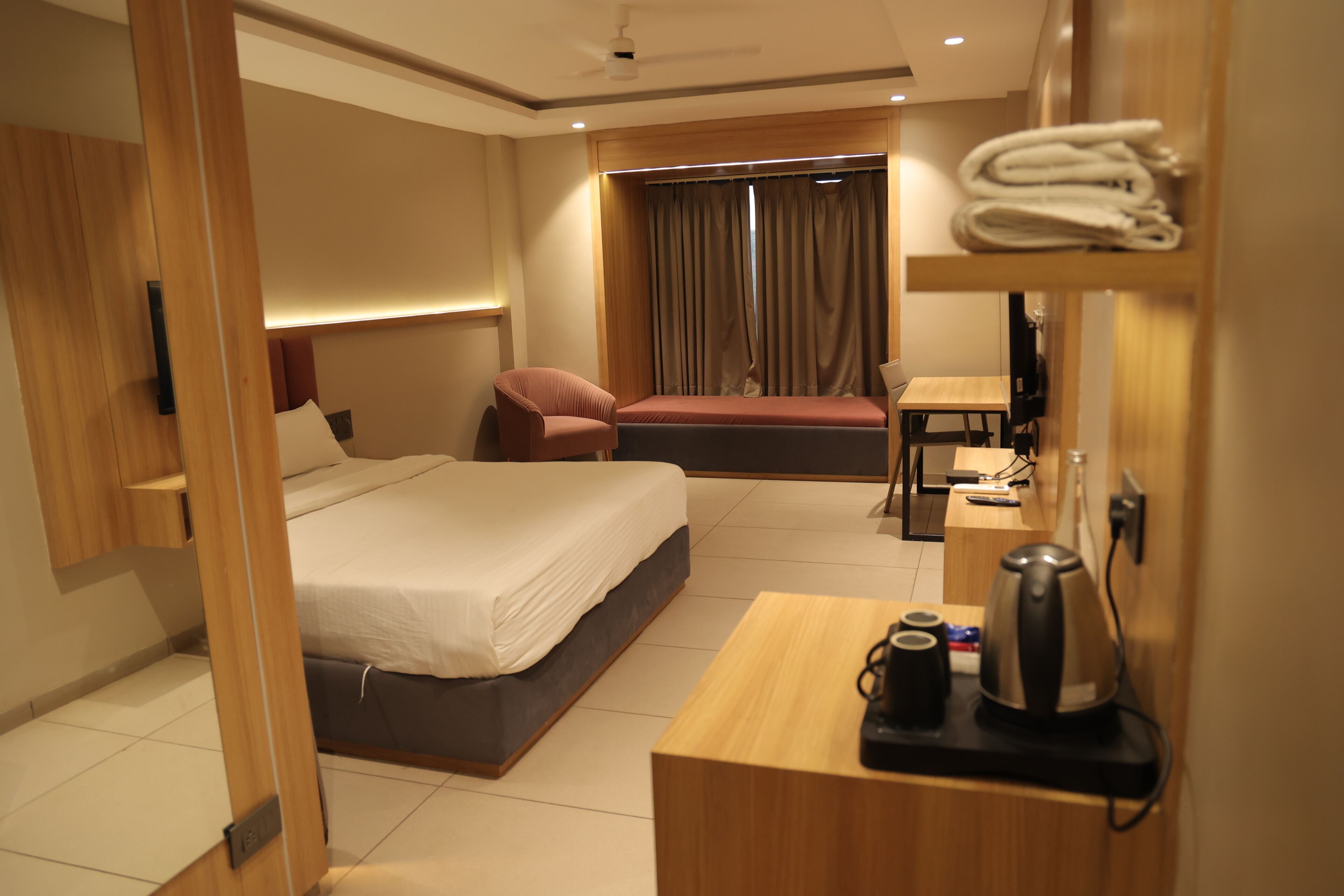 A hotel room with a bed, a desk, a chair, a TV, and a window with curtains.