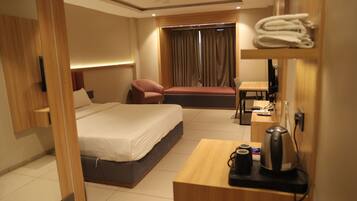 A hotel room with a bed, a desk, a chair, a TV, and a window with curtains.