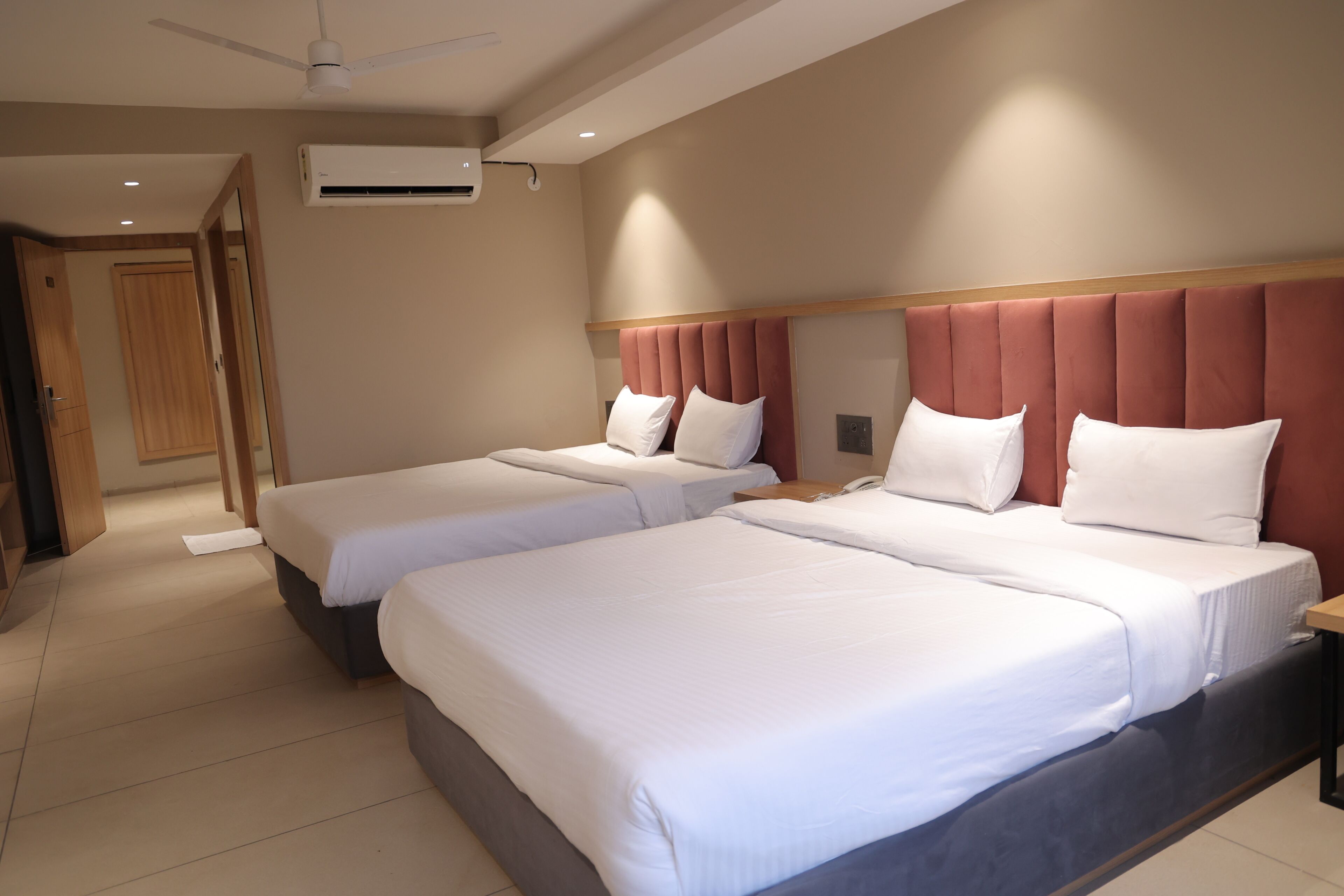 Une chambre d’hôtel avec deux lits, un ventilateur de plafond, un appareil de climatisation et une porte en bois.