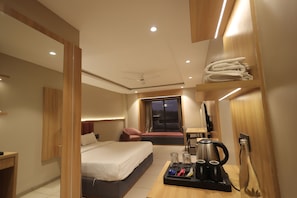A modern hotel room with a bed, seating area, and a kitchenette.