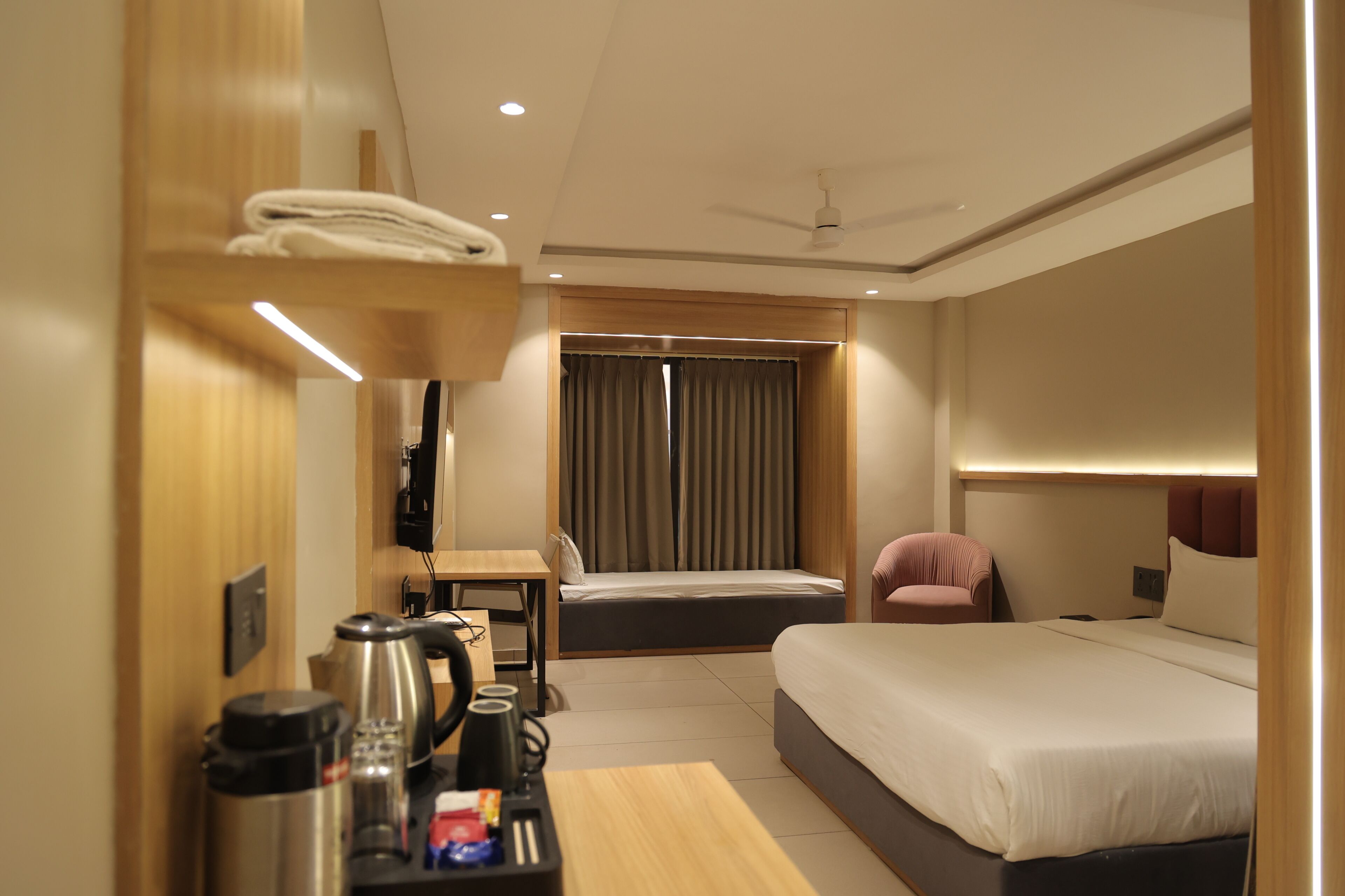 A hotel room with a bed, a desk, a chair, a coffee maker, and a TV.