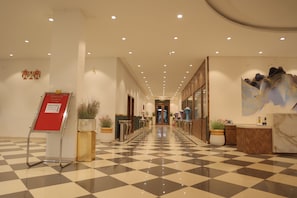 Un vestíbulo de hotel con piso a cuadros, una mesa de recepción y plantas en macetas.
