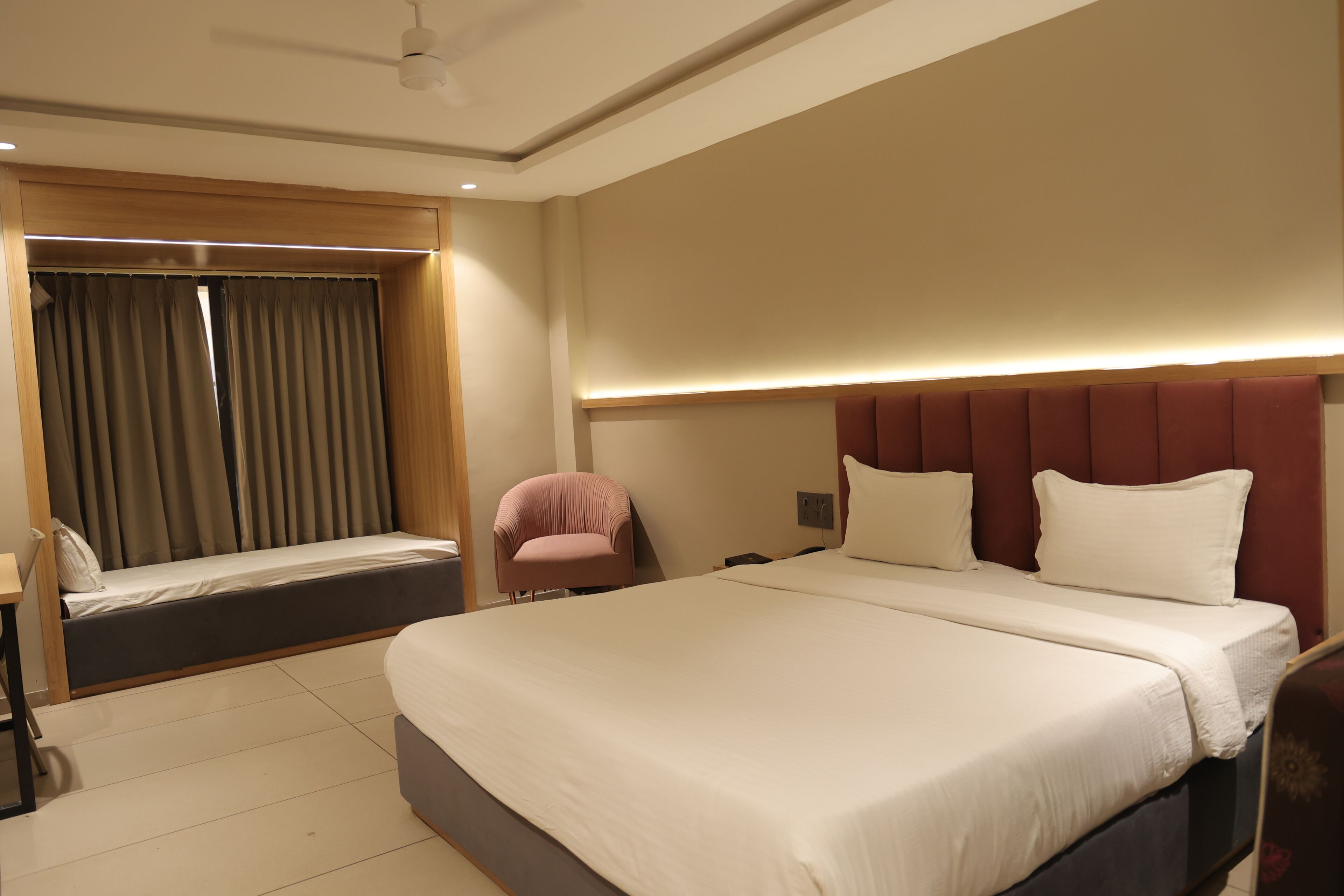 Habitación de hotel con una cama grande, un escritorio, una silla y un ventanal con cortinas.