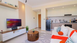 A modern living room with a flat-screen TV, a wooden coffee table, and a sofa with patterned cushions. - Luxury 1 Bedroom in Westlands Nairobi with Pool, Gym & Skyline Views (Nairobi)