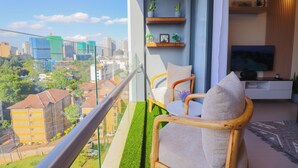 A balcony with a city view, a sofa, a TV, and shelves with plants. - Luxury 1 Bedroom in Westlands Nairobi with Pool, Gym & Skyline Views (Nairobi)