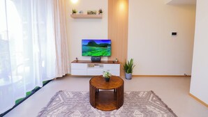 A living room with a TV, a round wooden coffee table, a patterned rug, a white cabinet, and a potted plant. - Luxury 1 Bedroom in Westlands Nairobi with Pool, Gym & Skyline Views (Nairobi)