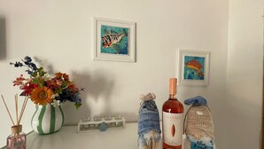 Ett bord med en flaska Garnet-vin, en dekorativ vas med blommor, en liten flaska handsprit och ett inramat konstverk på väggen.