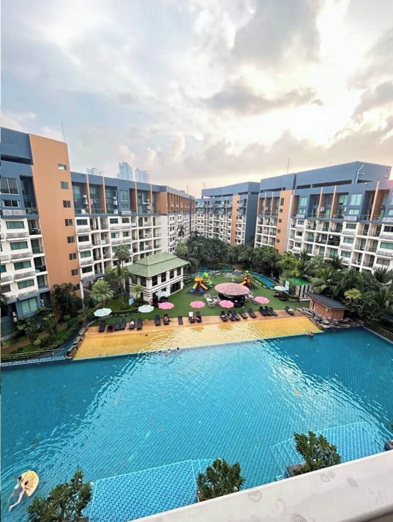 A residential building with a swimming pool, sun loungers, and a children's play area.