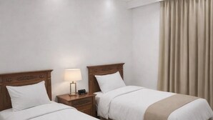 Una camera d'albergo con due letti, un comodino con una lampada e un'ampia finestra con tende.