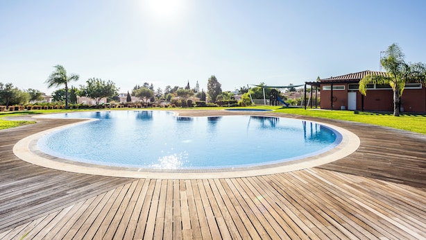Una piscina con muelle de madera, rodeada de vegetación y edificios.