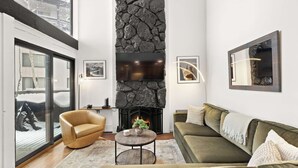 Una sala de estar moderna con chimenea de piedra, un sillón de cuero, un sofá verde y un ventanal grande.