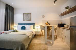 A modern hotel room with a bed, bedside table, lamp, and a kitchenette area. - Gateway to Modern Elegance (Bucharest)