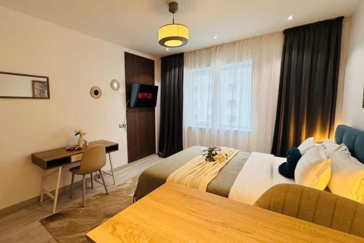 A hotel room with a bed, a desk, a chair, a TV, and a window with curtains.